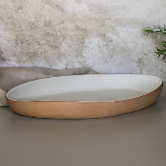 Oval ceramic dish with terracotta rim on a neutral background