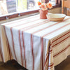 Table with a striped tablecloth, bowl, and flowers in a room with a window.