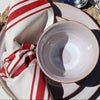 Dining table setting with plates, cutlery, and a cracker on a red and white striped tablecloth.