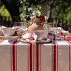 Dining table set with red and white striped tablecloth, glasses, and decorative items outdoors.