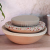 Stack of ceramic bowls with floral and plain muslin dish covers on a wooden surface