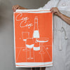Person holding an orange towel with white wine graphics and 'Cin Cin' text.