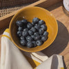 Small ochre yellow bowl filled with blue berries in an oak tray 