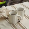White mugs with tea and plate with rusks being placed on striped tablecloth
