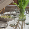 Person pouring water in stemmed glass from sand coloured ceramic jug all set on striped table cloth