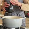 Person using salt pot to sprinkle salt into pot 