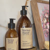 Person pumping hand wash into hand - brown glass bottle with craft label reading Kitchen Hands' Natural Hand Wash 